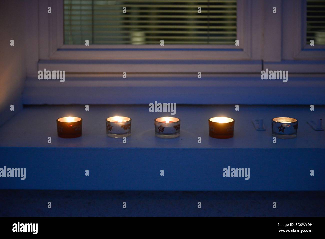 Am Abend werden mehrere kleine Kerzen auf der Fensterbank eines Hauses angezündet Stockfoto