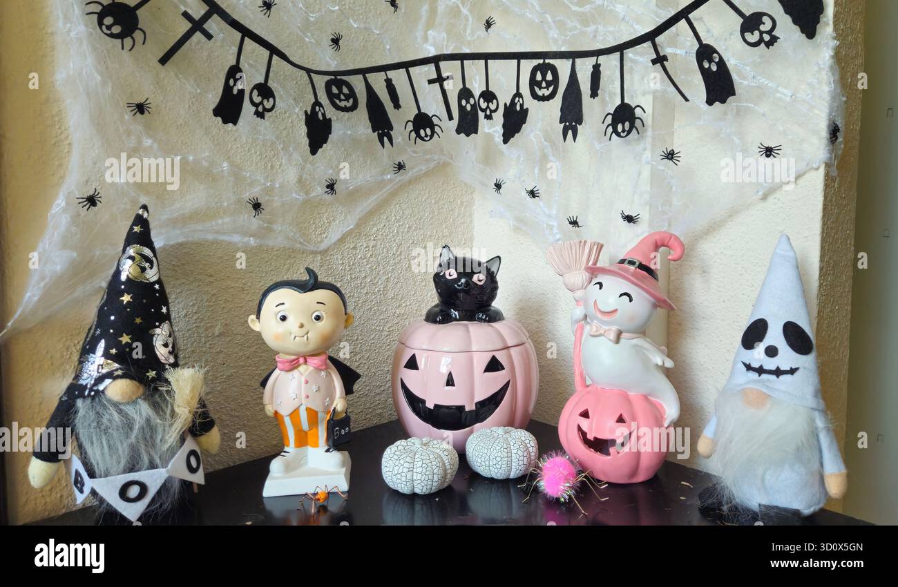 Gruselige niedliche Halloween-Wohnkultur mit Gnomen, Vampirpuppe, schwarzer Katze und Geisterfigur vor einem gefälschten Spinnennetz-Hintergrund Stockfoto