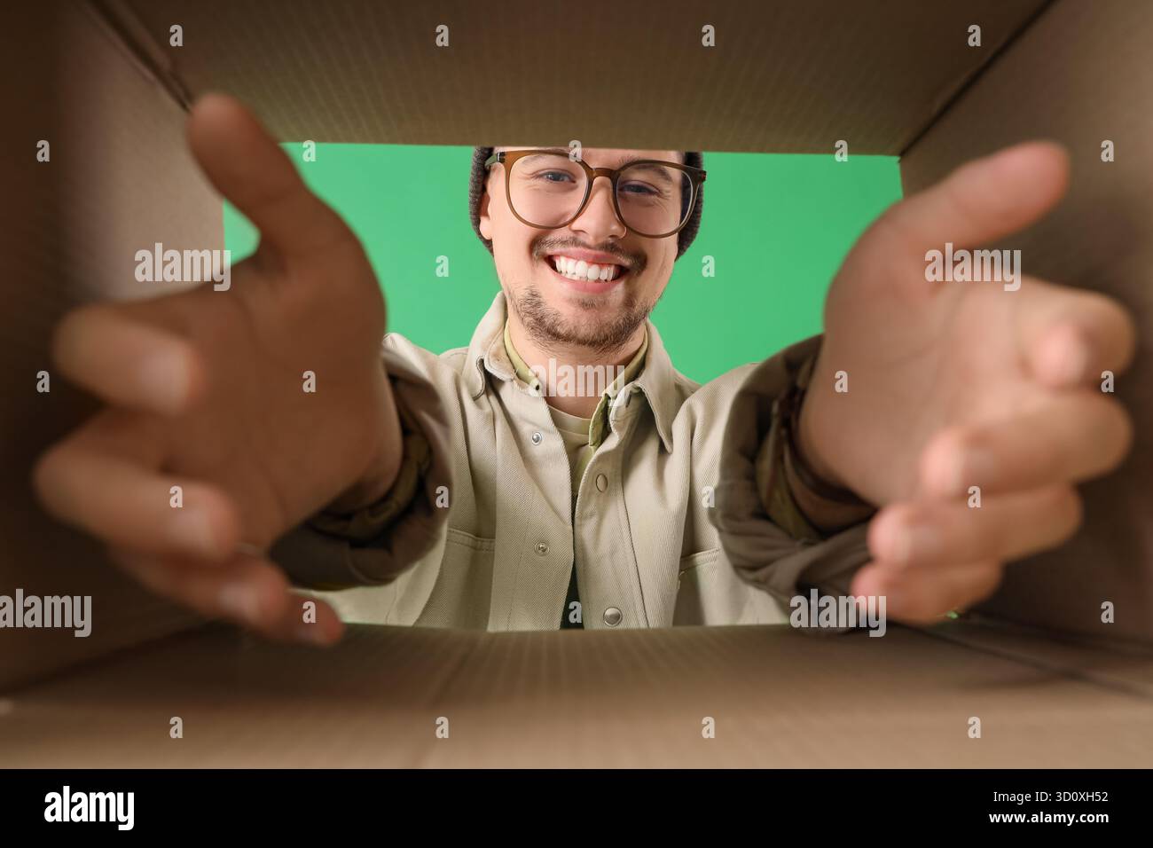 Schöner Mann mit offenem Karton auf grünem Hintergrund, Blick von innen Stockfoto