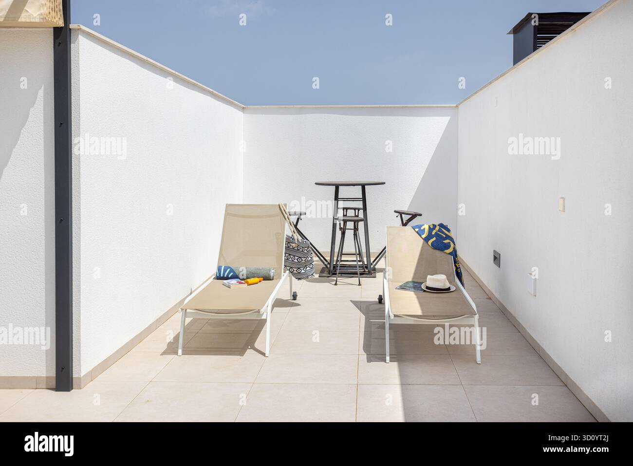 Zwei beigefarbene Loungesessel mit Bartisch und minimalistischer Einrichtung auf einer privaten, sonnigen Dachterrasse, ideal zum Entspannen und Sonnenbaden. Stockfoto
