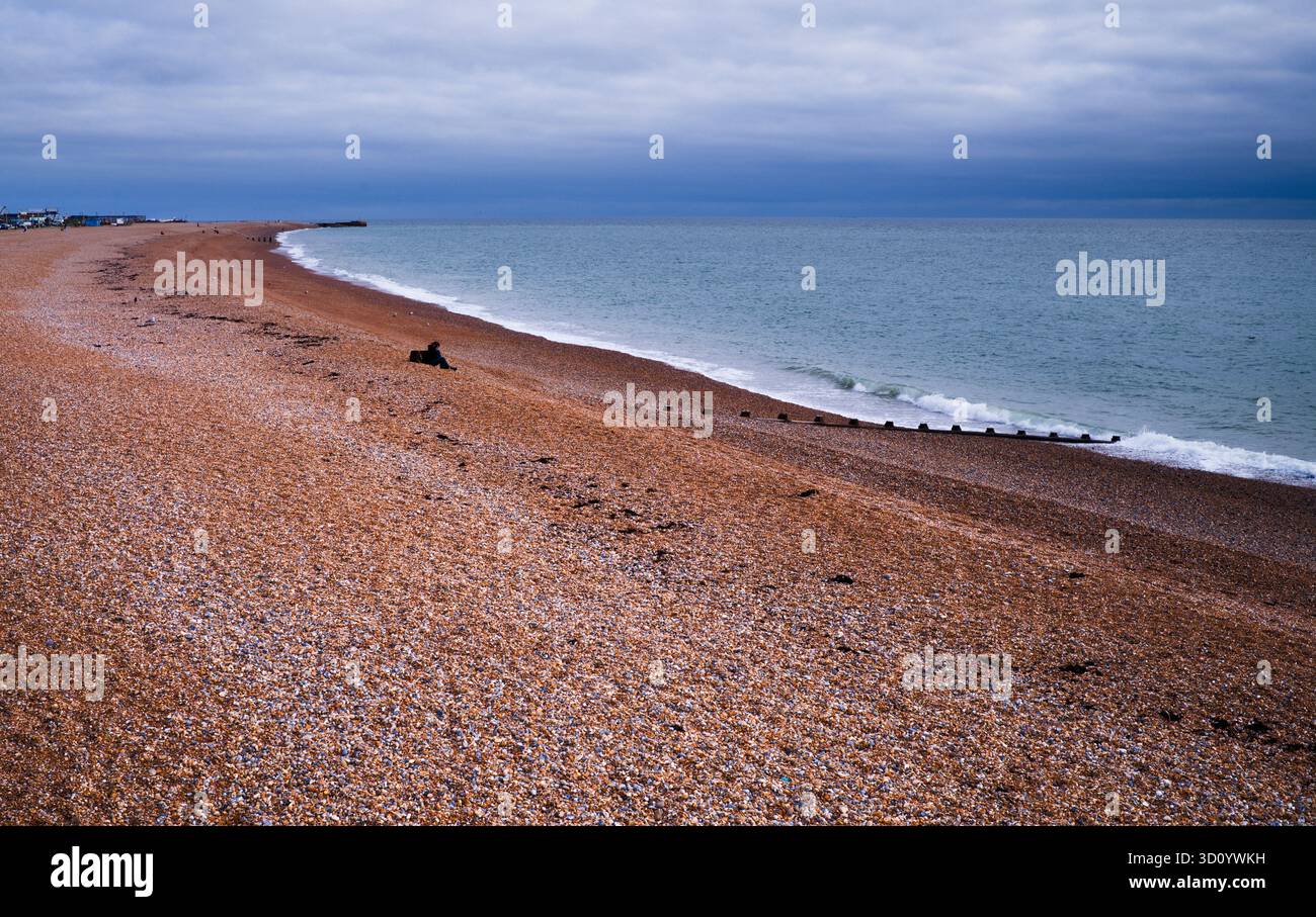 Mann, der allein mit Kopfhörern am Strand von Hastings sitzt Stockfoto