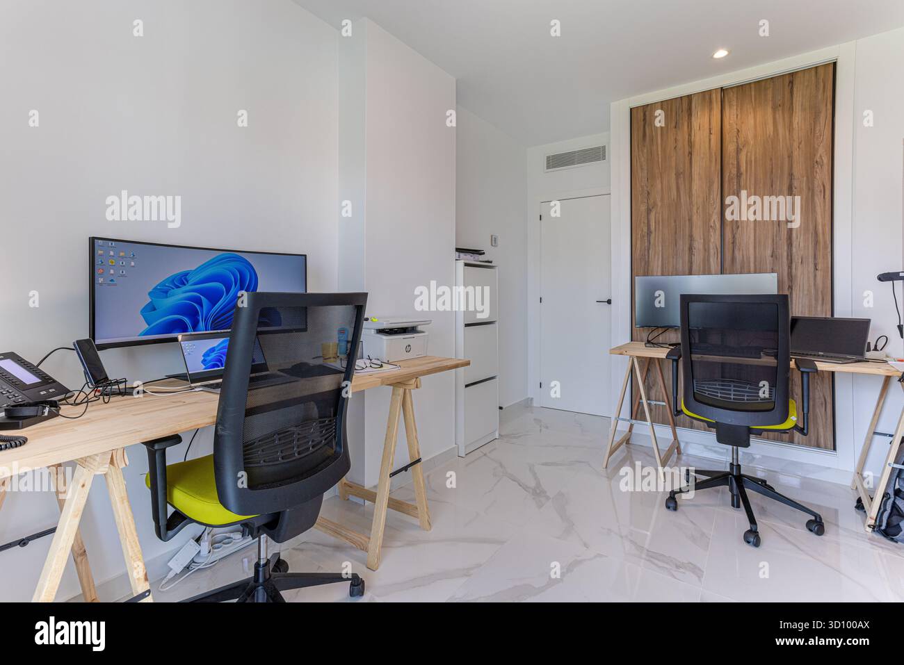 Funktionales Home Office mit zwei Arbeitsplätzen, Holzmöbeln, ergonomischen Stühlen und großen Bildschirmen in einem sauberen, modernen Raum. Stockfoto