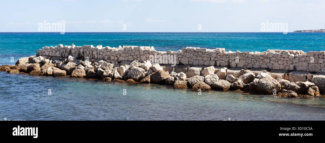 Felsige Steinmauern, die die Küste von La Caletta, Siniscola, Sardinien, Italien, schützen. Stockfoto