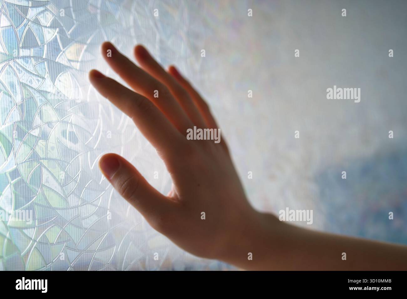 Menschliche Hand berührende gemusterte Glasoberfläche mit weichem natürlichem Licht und abstrakter Hintergrundstruktur Stockfoto