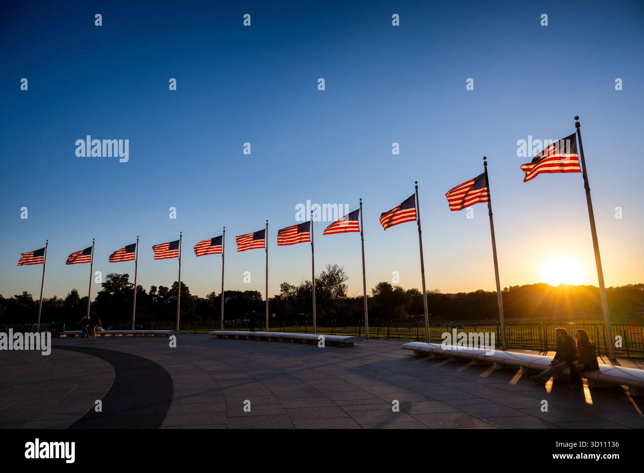 Washington DC // WASHINGTON DC – Eine Reihe amerikanischer Flaggen fliegt auf der National Mall in Washington D.C. gegen die untergehende Sonne und erzeugt einen goldenen Glanz und markante Schatten. In dieser bedeutenden Gegend befinden sich zahlreiche nationale Denkmäler und Denkmäler, darunter das nahe gelegene World war II Memorial. Die National Mall wird vom National Park Service verwaltet und dient als zentraler Treffpunkt für öffentliche Veranstaltungen und Demonstrationen. Stockfoto