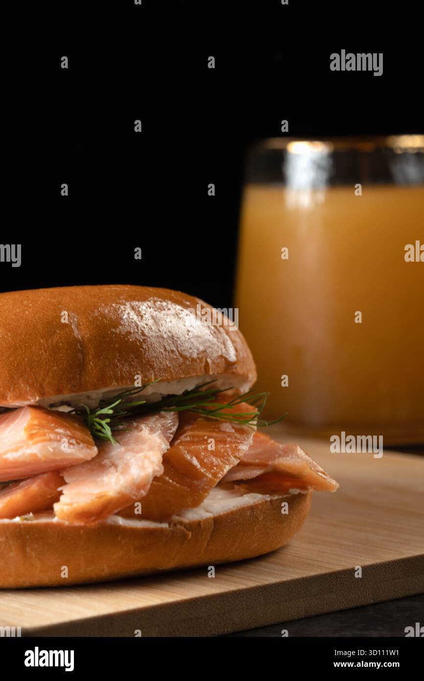 Ein Sandwich mit Lachs und Dill sitzt auf einem hölzernen Schneidebrett neben einem Glas Saft Stockfoto