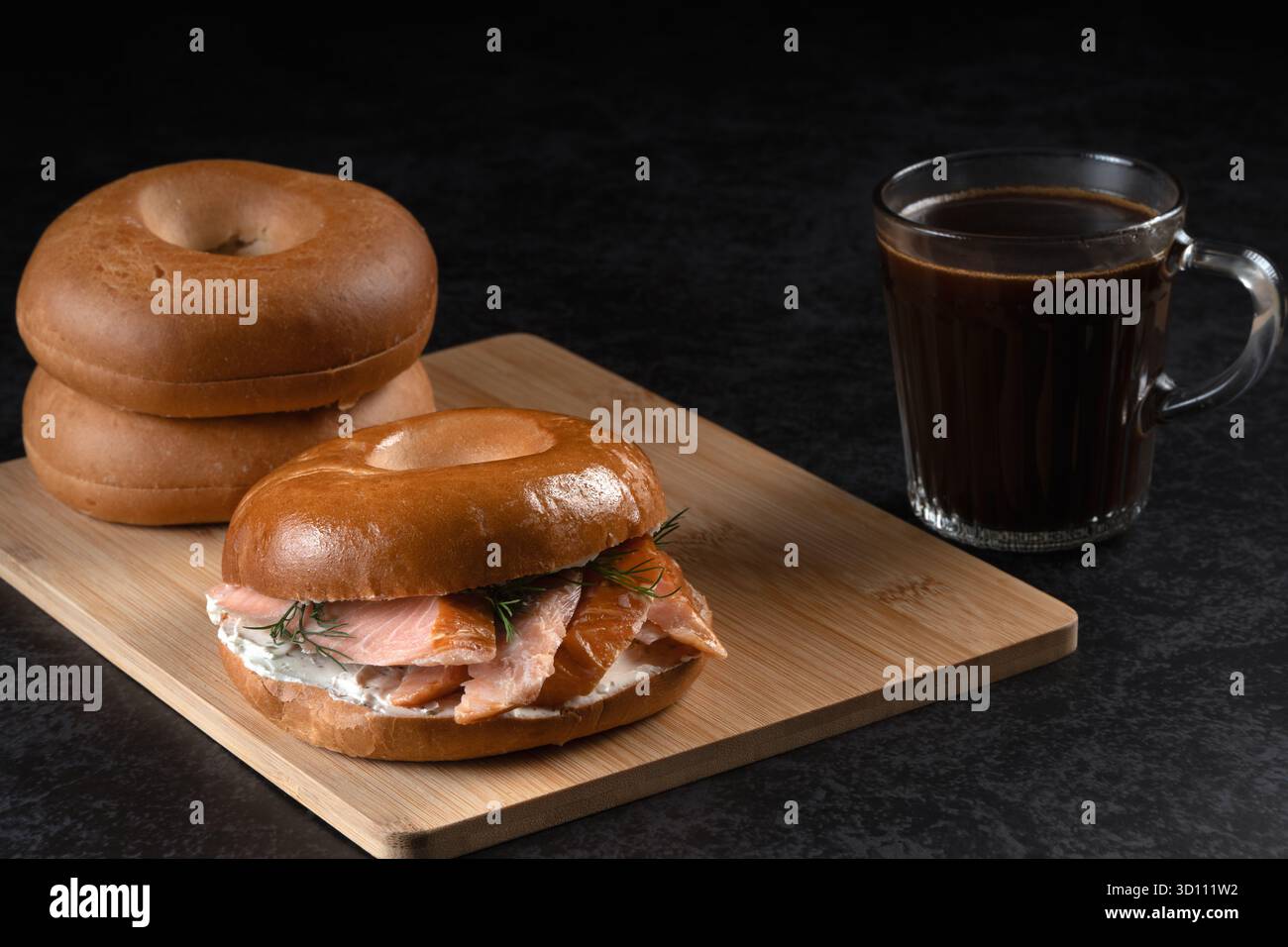 Ein Sandwich mit Lachs und Dill liegt auf einem Holzbrett neben einer Tasse Kaffee. Das Sandwich wird auf einem Holzbrett platziert und der Kaffee ist in einem gla Stockfoto