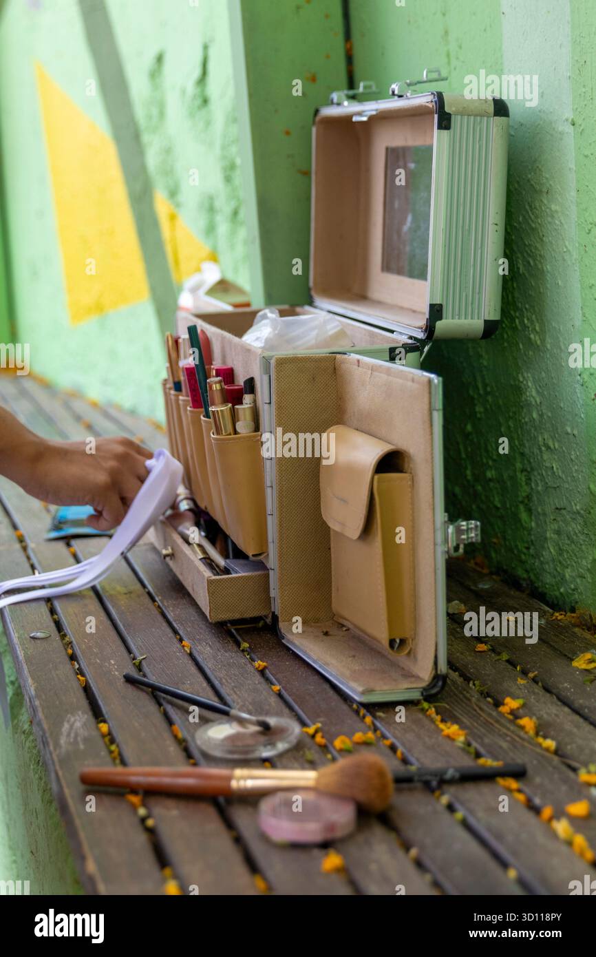 Professioneller Make-up-Künstler öffnet eine tragbare Kosmetiktasche mit Bürsten und verschiedenen Kosmetikprodukten auf einer Holzbank Stockfoto