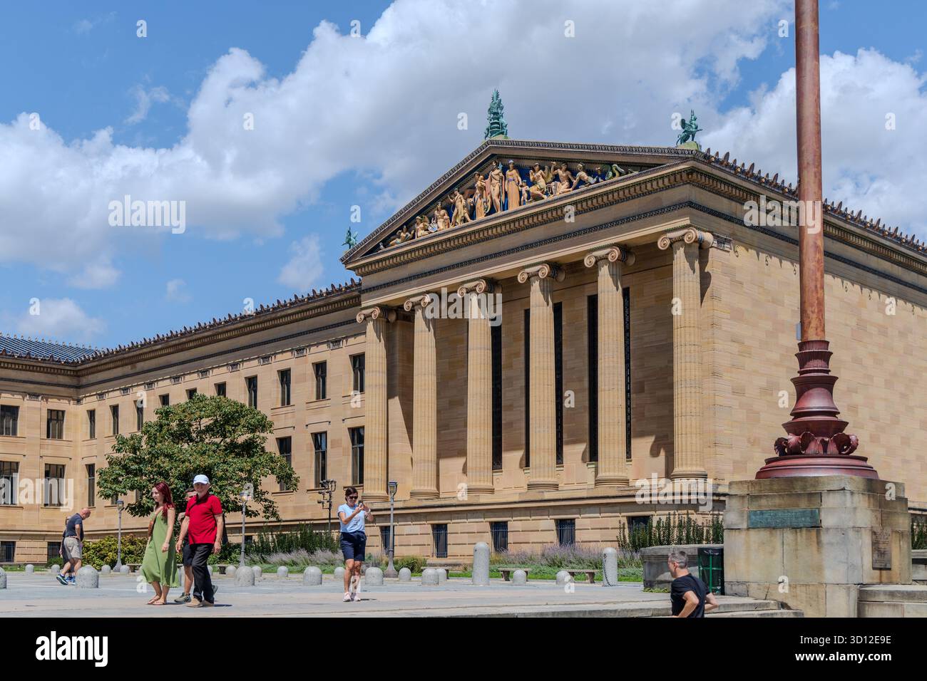 Eine Gruppe von Menschen läuft an einem großen Philadelphia Museum of Art mit einem hohen Stab davor vorbei. Das Gebäude hat ein klassisches Design und ist surr Stockfoto