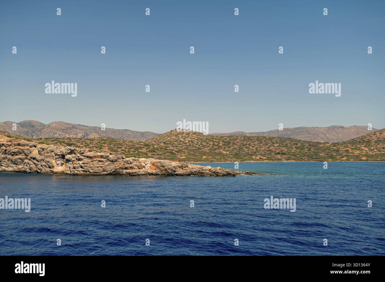 Wellen schlagen sanft gegen das felsige Ufer, während die Sonne auf Kreta hell scheint Stockfoto