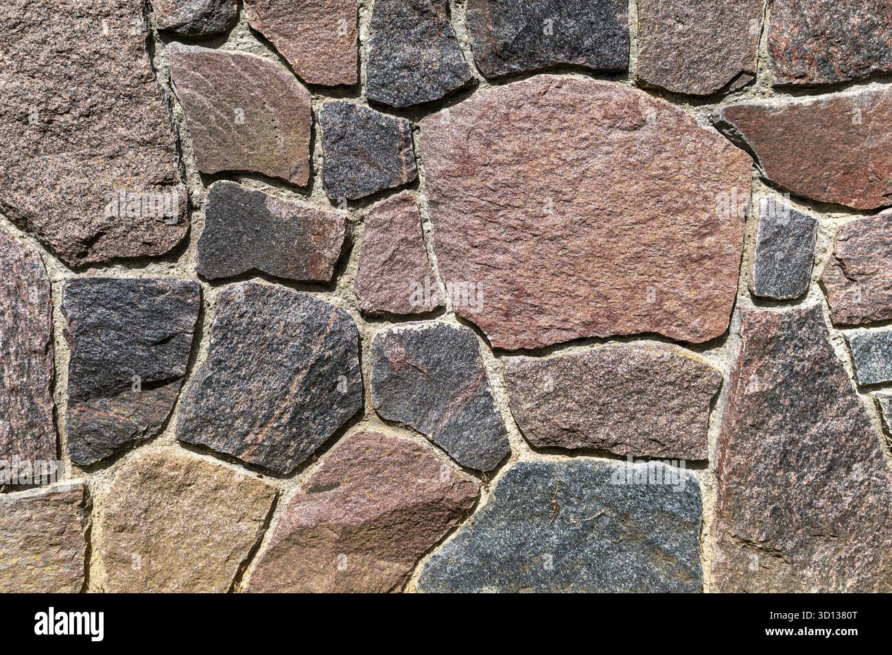 Eine rustikale Steinmauer zeigt verschiedene Formen und Töne von Natursteinen, die harmonisch angeordnet sind Stockfoto