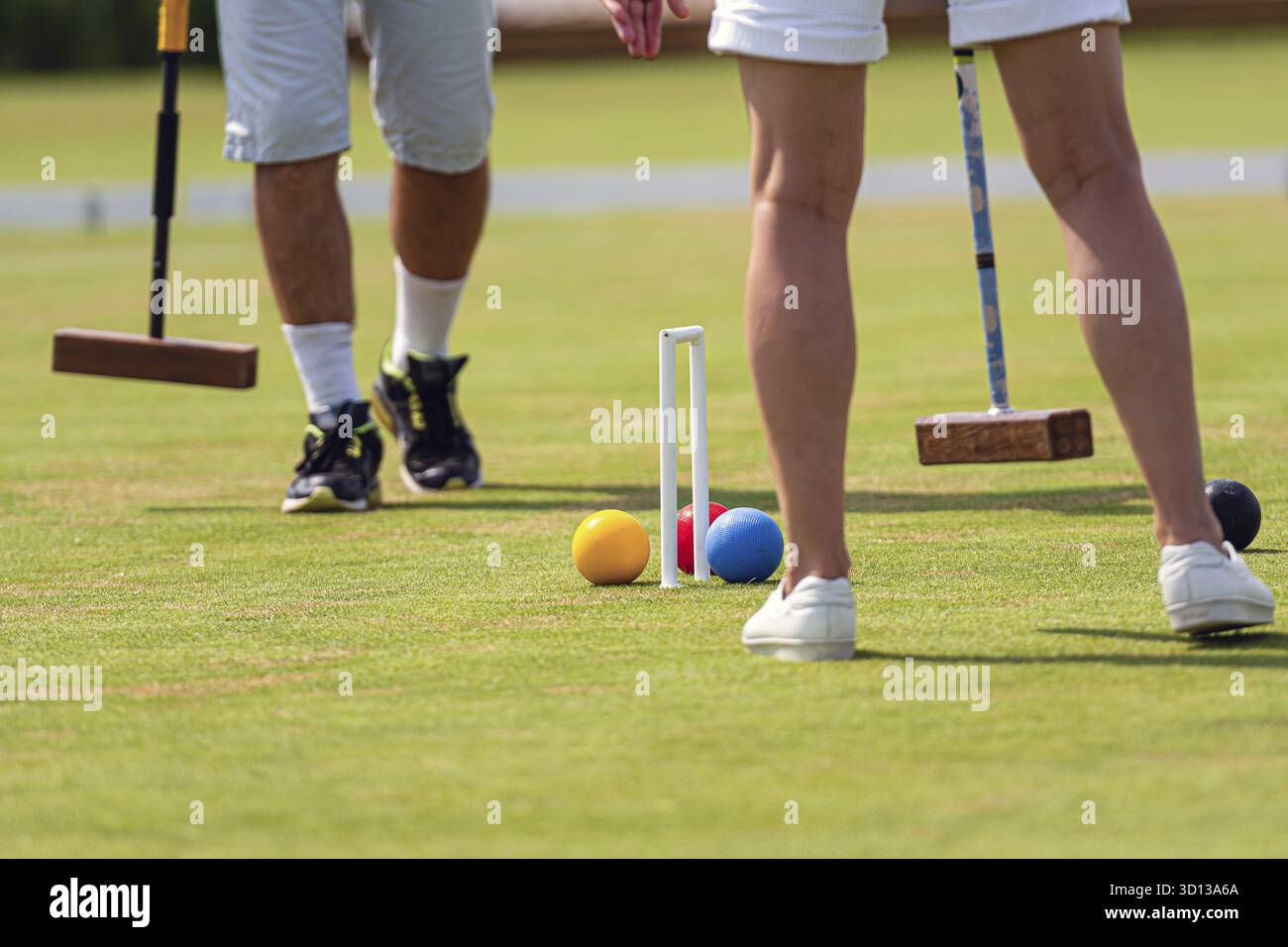 Zwei Personen spielen mittags ein lebhaftes Krocketspiel auf gut gepflegtem Gras Stockfoto