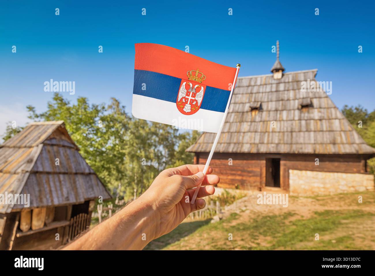 Hand hält die serbische Nationalflagge in einer traditionellen ländlichen Umgebung, symbolisiert Patriotismus und Erbe Stockfoto