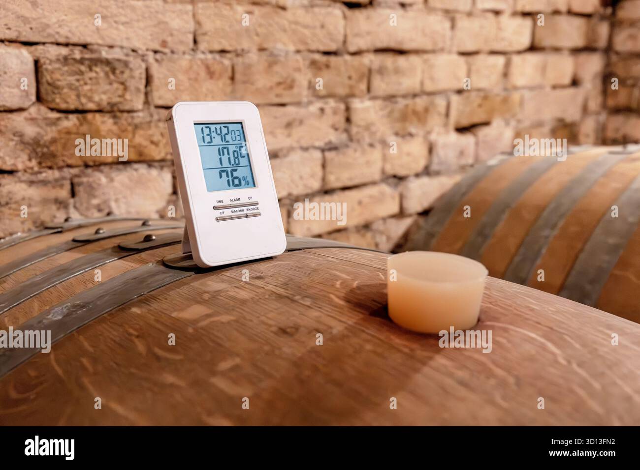 Digitales Thermometer auf einem Eichenfass, das genaue Temperatur- und Feuchtigkeitsmessungen für eine optimale Weinreifung in einem rustikalen Weinkeller ermöglicht Stockfoto