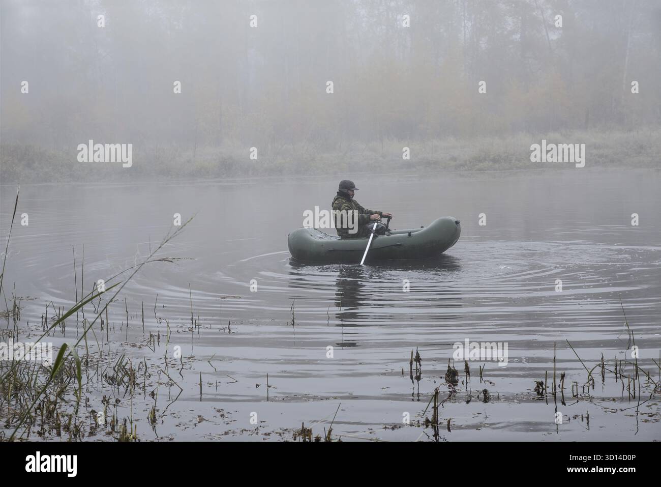 Ein Mann in einem Boot, der im Nebel auf dem See schwimmt Stockfoto