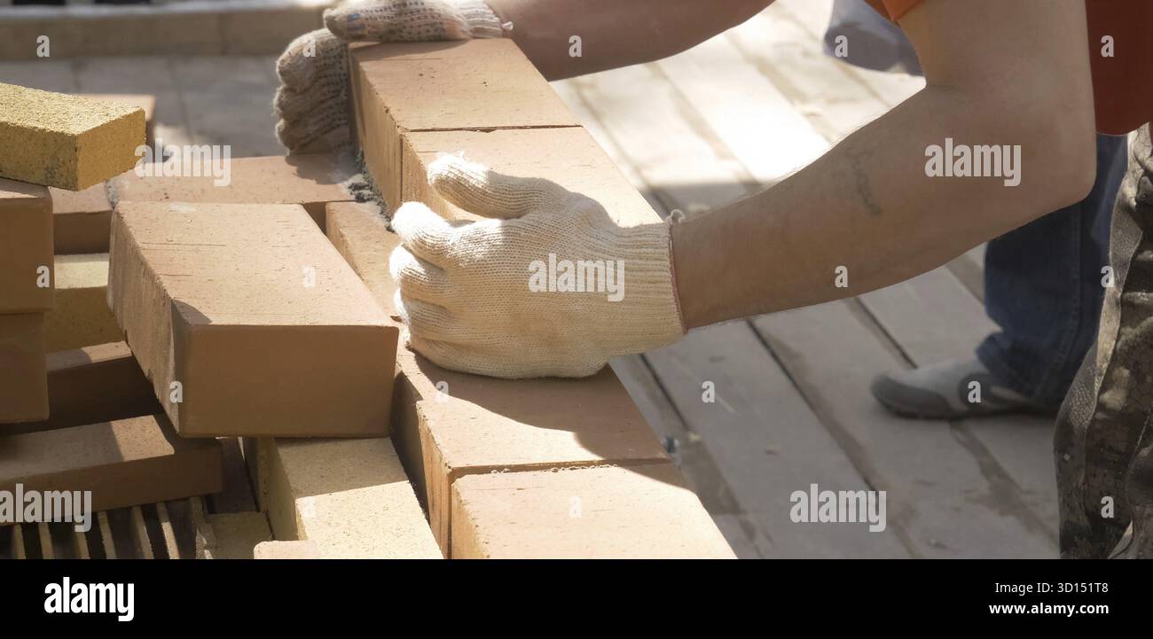 Ein Mann baut eine Mauer. Brick hat die Lösung aufgesetzt. Bau eines Backsteinhauses Stockfoto