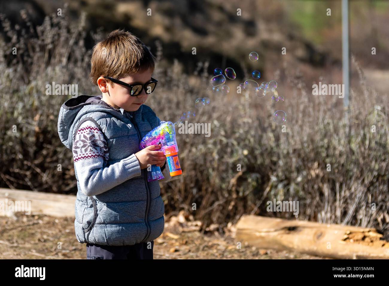 Ein Kind mit einer Sonnenbrille genießt es, mit einem Luftpolsterspielzeug in einer natürlichen Umgebung Luftblasen zu erzeugen. Stockfoto