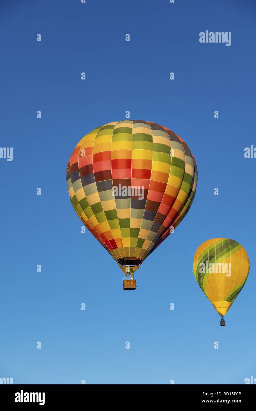 Guadix, Granada - Spanien - 24.01.2024: Zwei bunte Heißluftballons steigen in den klaren blauen Himmel. Einer hat ein buntes kariertes Muster, der andere ist y Stockfoto