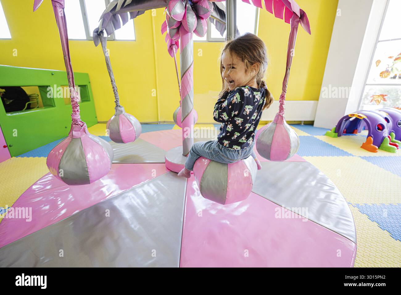 Glückliches Mädchen, das auf dem Spielplatz im Indoor-Spielzentrum spielt, schaukel auf der Palme Stockfoto