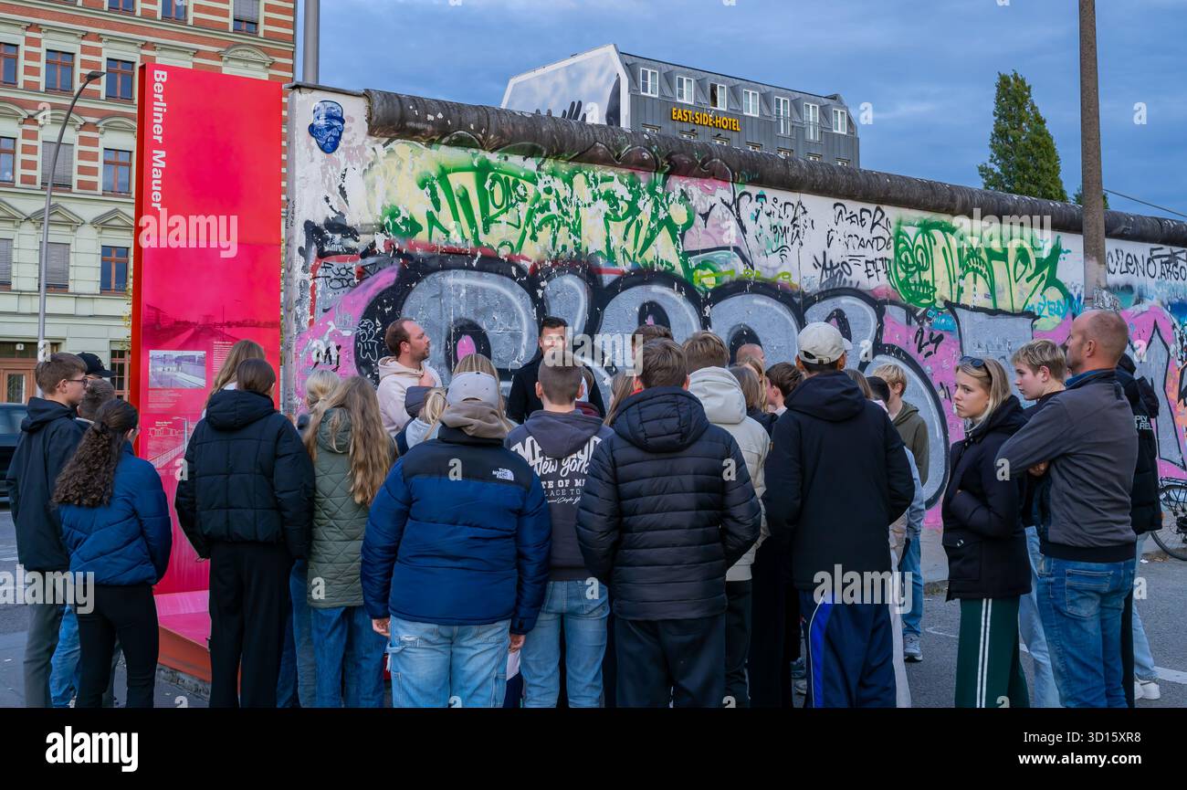 Eine Gruppe von Touristen hört einem Reiseleiter in der Berliner Wall East Side Gallery in Berlin, Deutschland. Stadttourismus, Gruppe von Touristen, Tourgruppe. Stockfoto