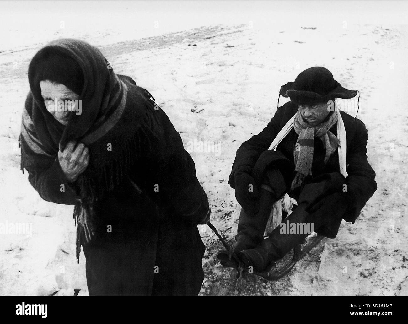 LENINGRAD, RUSSLAND - 07. Februar 1942 - eine ältere Frau zieht während der Belagerung Leningrads im Zweiten Weltkrieg einen Mann auf einem Schlitten mit sich. Der genaue Ort dieses Fotos ist nicht bekannt, obwohl es von der "Straße des Lebens" stammen könnte - durch die viele Flüchtlinge aus der Belagerung geflohen sind - Foto: Geopix Stockfoto