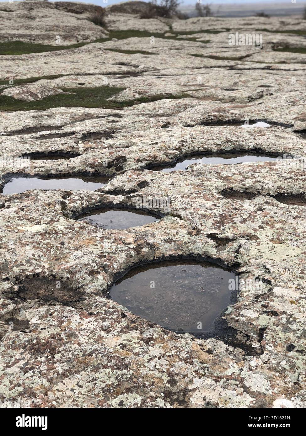 Cluster kreisförmiger Bewitterungsgruben, gefüllt mit Regenwasser auf lichenem Grundgestein, Provinz Ardabil, Iran. Stockfoto