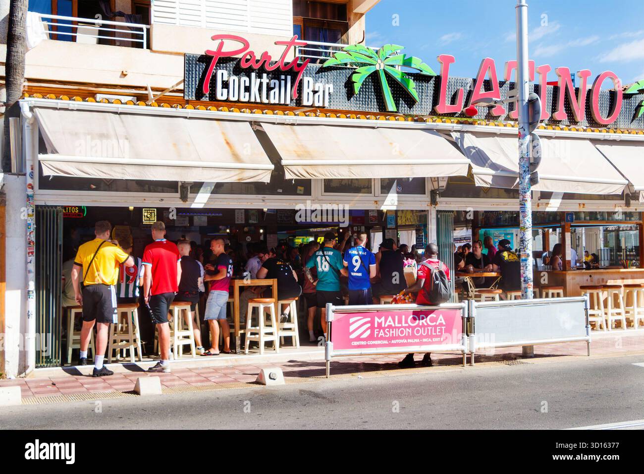 In einer Cocktailbar im Freien versammelten sich viele Menschen mit Fußballtrikots auf einer belebten Straße in S'an pastilla Mallorca mit Partyschildern Stockfoto