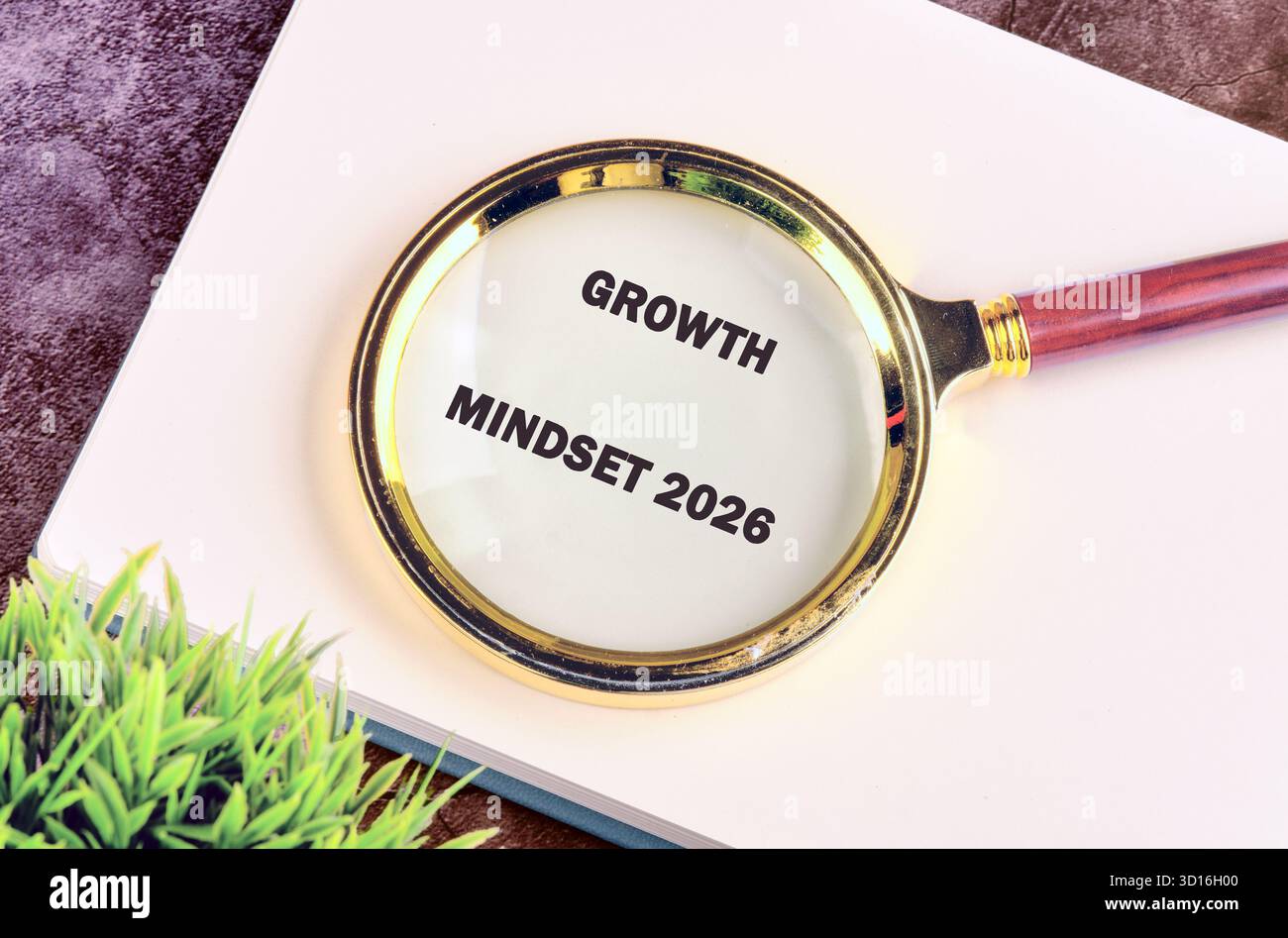 Eine Lupe lenkt die Aufmerksamkeit auf das Growth Mindset 2026, das auf Papier gedruckt wird. Es liegt auf einem Notizbuch, mit einer kleinen grünen Pflanze in der Nähe, die für Fo steht Stockfoto
