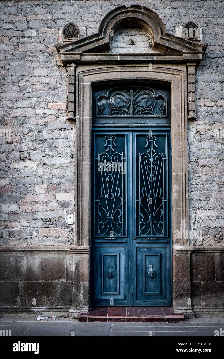 Verzierte Vintage-blaue Holztür mit schmiedeeisernen Details in einem Steingebäude mit klassischen architektonischen Elementen Stockfoto