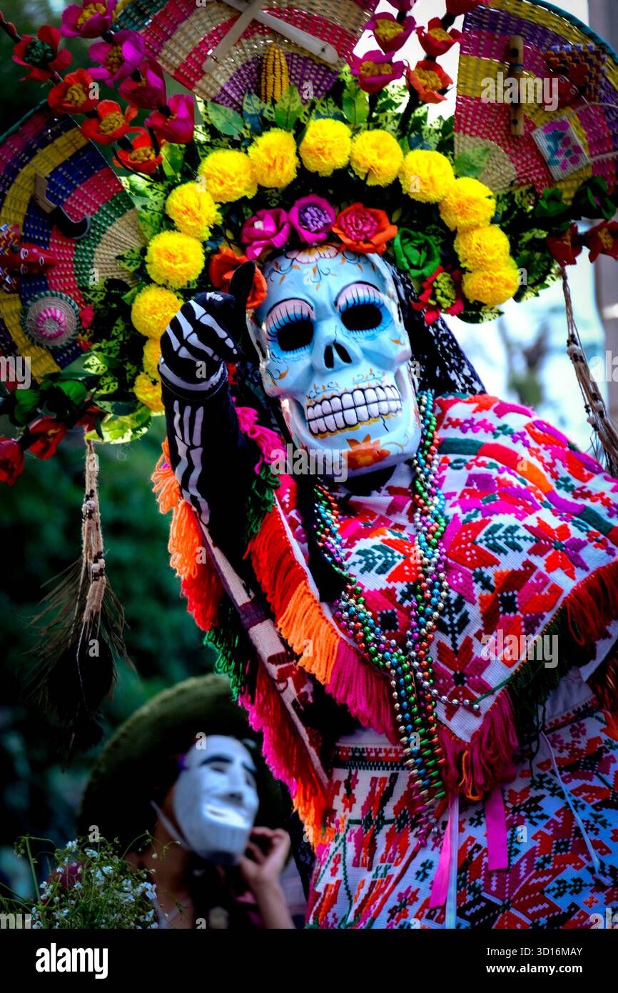 Die Person trägt ein traditionelles besticktes Kostüm und eine Totenkopfmaske, die den Tag der Toten feiert, mit einem farbenfrohen Kopfschmuck und Perlen Stockfoto