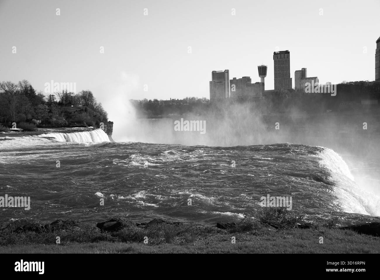 Schwarz-weiß-Blick auf die American Falls mit aufsteigendem Nebel und die Skyline der Niagarafälle, Ontario jenseits des Flusses Stockfoto