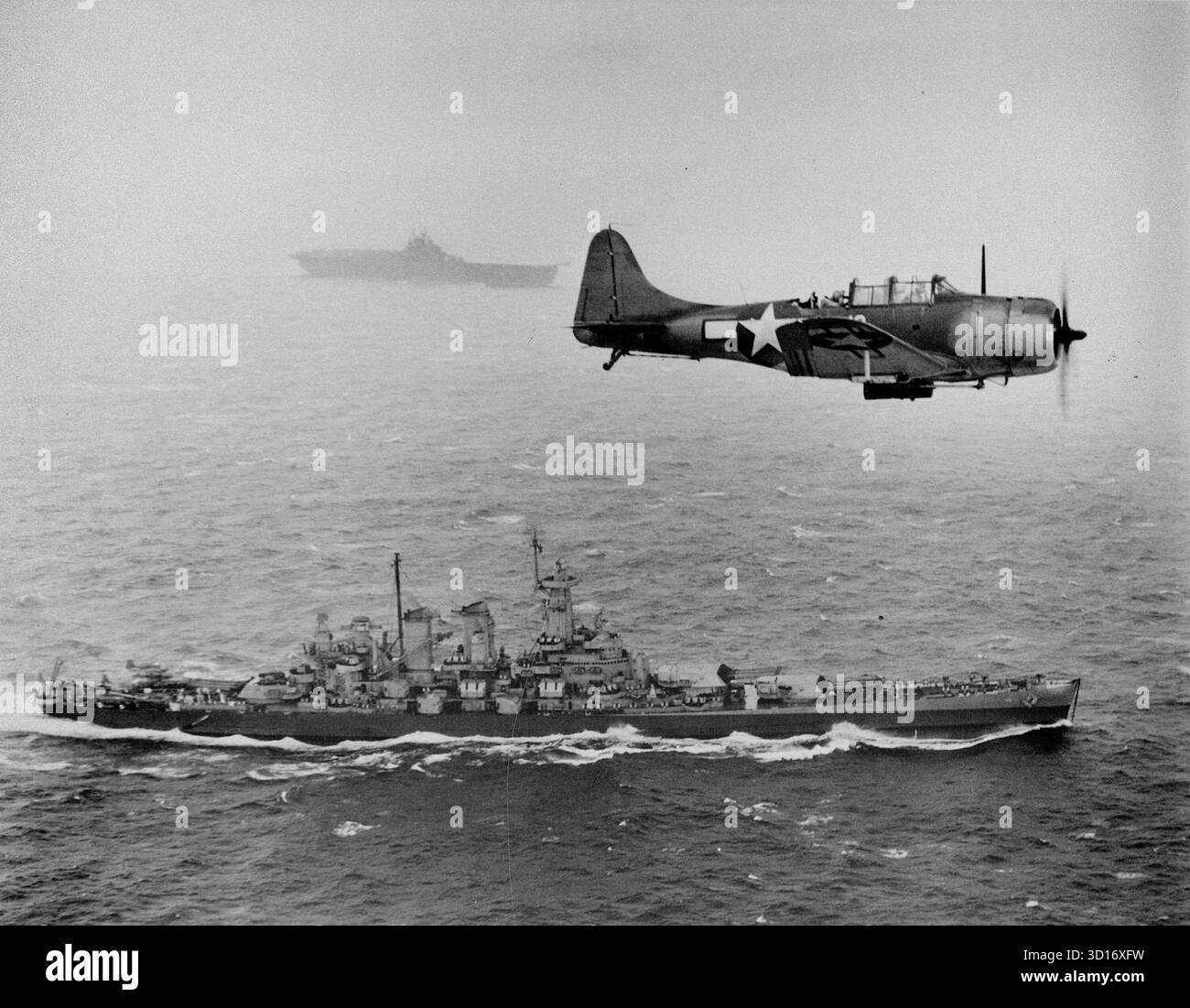 VOR DEN GILBERT-INSELN, PAZIFIK - 12. November 1943 - Eine US-Navy Douglas SBD-5 Dauntless der Bombenstaffel VB-16 fliegt eine U-Boot-Patrouille tief über dem Schlachtschiff USS Washington (BB-56) auf dem Weg zur Invasion der Gilbert-Inseln während des Zweiten Weltkriegs. Das Schiff im Hintergrund ist USS Lexington (CV-16), der Heimträger des Flugzeugs - Foto: Geopix/US Navy Stockfoto