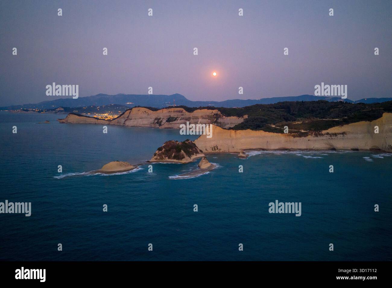 Breites Luftpanorama des Vollmondes, der über Kap Drastis, Korfu, Griechenland aufsteigt. Die weißen Klippen und die Küste sind von der Dämmerung beleuchtet und weit entfernt Stockfoto