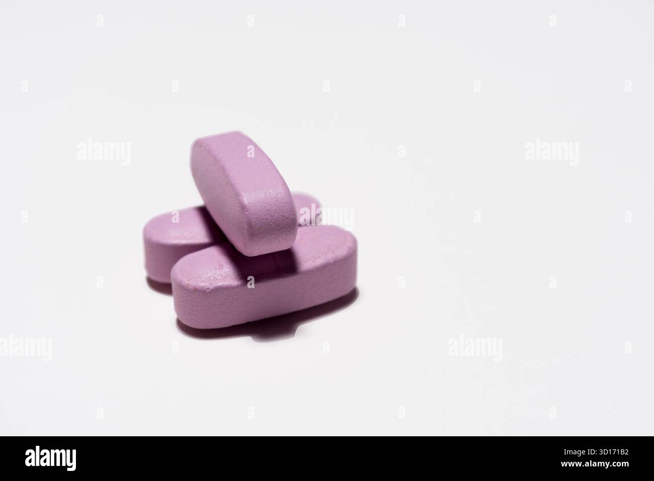 Arzneimittel, drei längliche rosa Tabletten auf weißem Hintergrund, angeordnet, wobei eine die anderen zwei berührt. Stockfoto