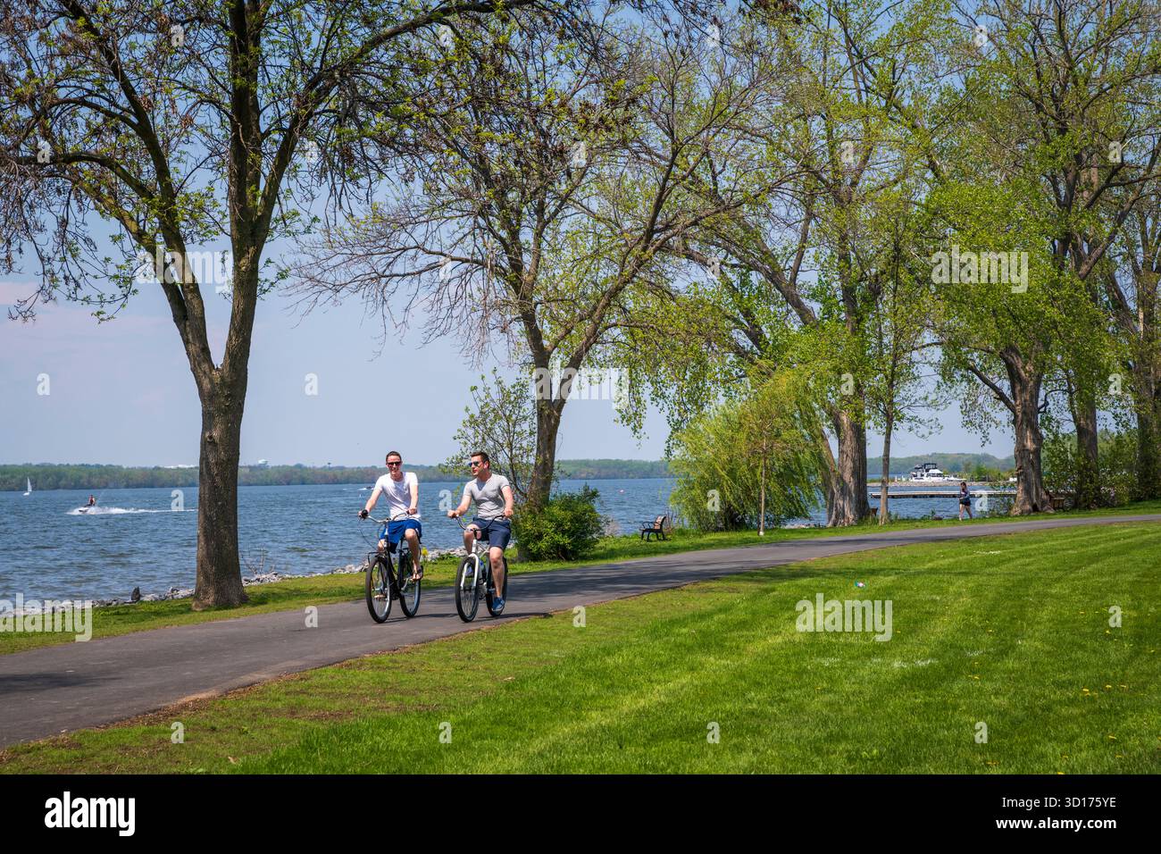 Syracuse, NY USA - 18. Mai 2019: Biker auf baumgesäumten Wegen im Onondaga Lake State Park. Stockfoto