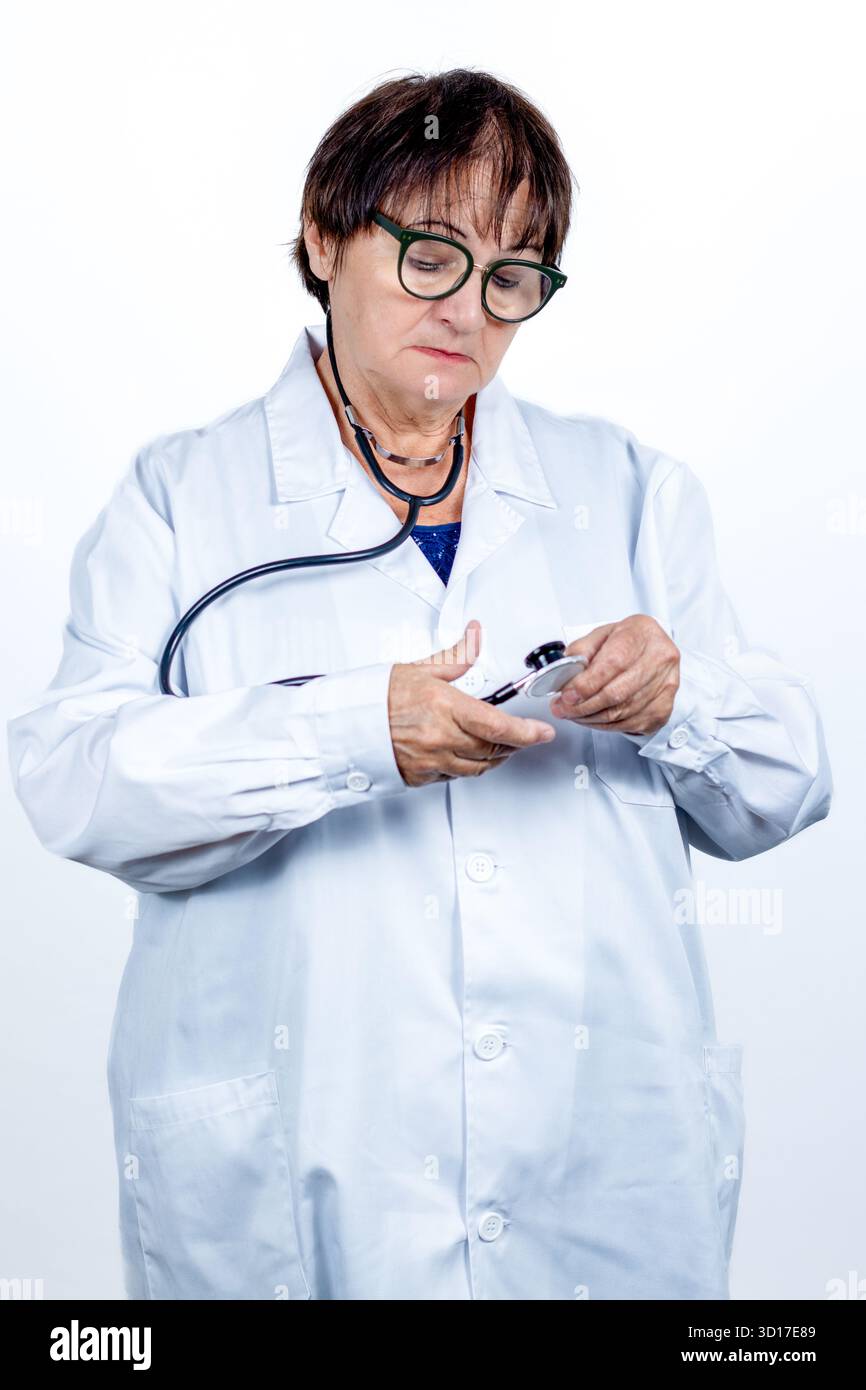 Ältere Ärztin mit weißem Labormantel und Brille, hält und passt ihr Stethoskop an, symbolisiert Gesundheit, Professionalität Stockfoto