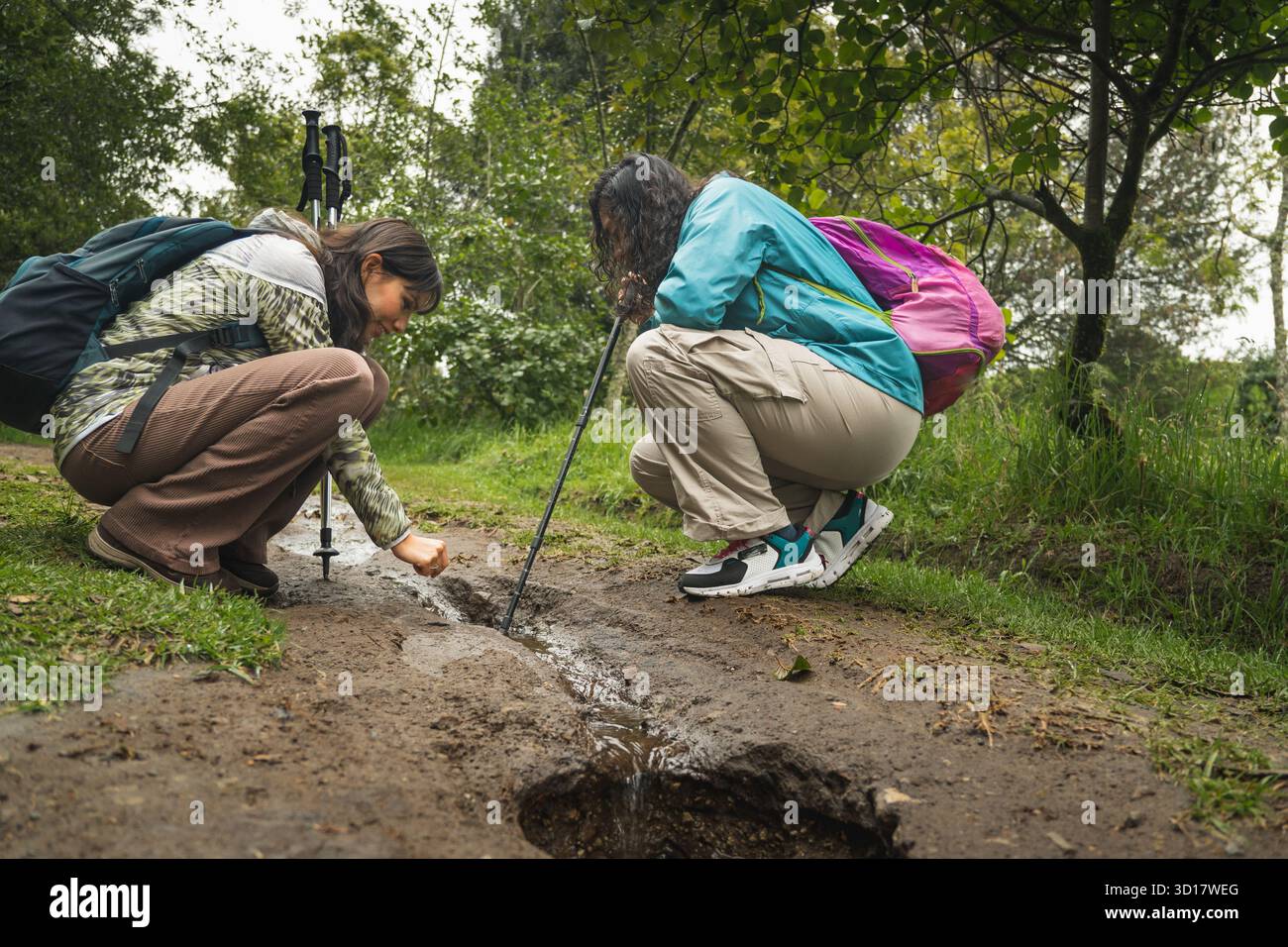 Zwei Frauen beobachten einen kleinen Bach auf einem schlammigen Pfad während ihrer Naturwanderung Stockfoto
