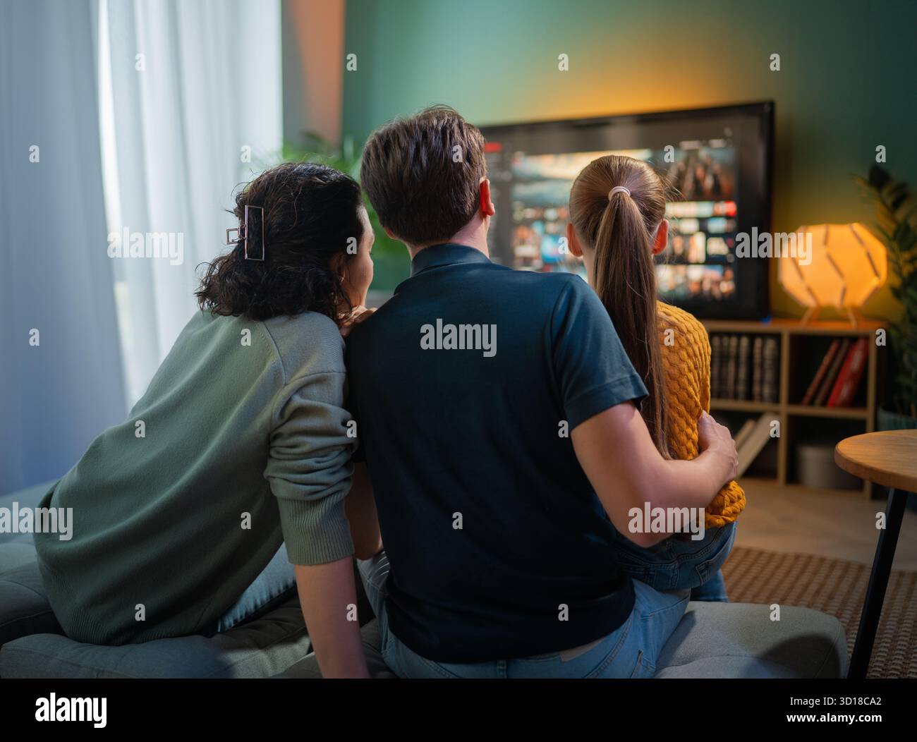 Glückliche Familie, die Zeit miteinander verbringt. Mutter, Vater und Kind schauen fern, Filme am Abend zu Hause. Stockfoto