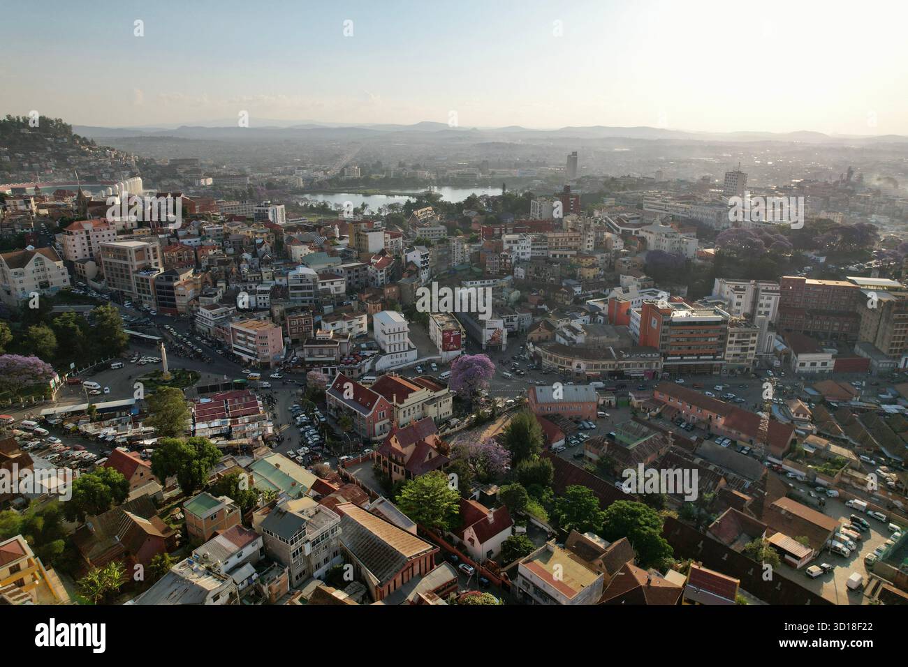 Sonnenuntergang Panorama des Gare de Soarano, Avenue de l’Indépendance und Kreisverkehr Soarano mit Jacarandabäumen und dem Stadtschild von Antananarivo am Hügel. Stockfoto