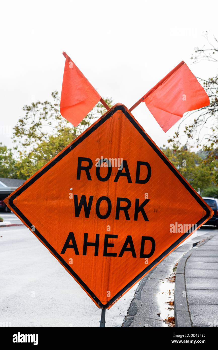 Orangefarbenes Verkehrswarnschild, das Kraftfahrzeuge auf vor Straßenarbeiten warnt und bereit ist, anzuhalten. Stockfoto