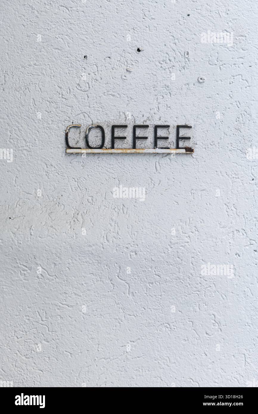 Weiße Stuckwand mit einem Metall, einem erhöhten Buchstaben, das Kaffee anwarnt. Stockfoto
