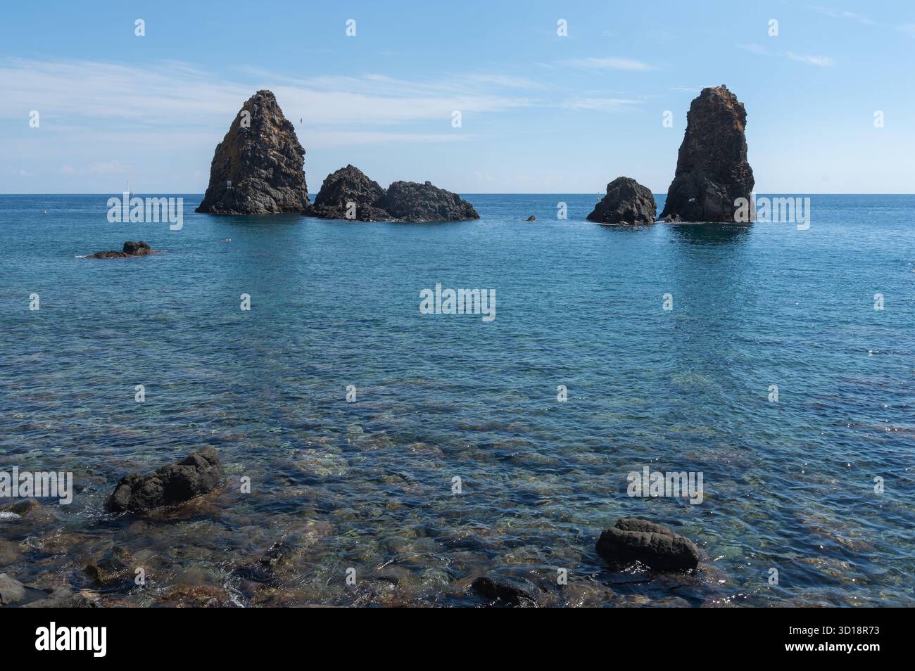 Das klare blaue Wasser an der Küste von ACI Trezza in Sizilien, mit einigen der vulkanischen Meeresstapel, die dort bewundert werden können Stockfoto