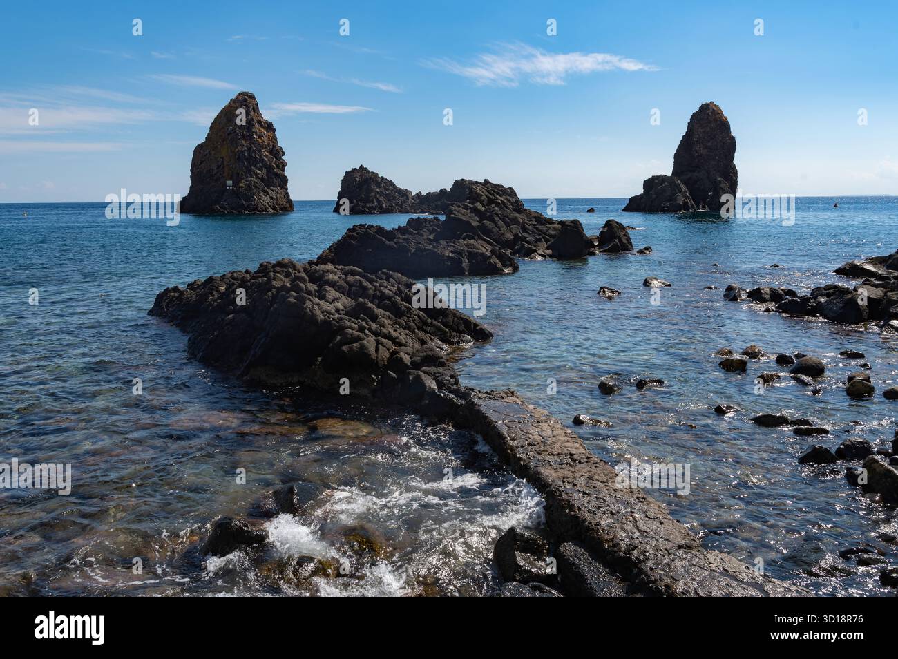 Das klare blaue Wasser an der Küste von ACI Trezza in Sizilien, mit einigen der vulkanischen Meeresstapel, die dort bewundert werden können Stockfoto