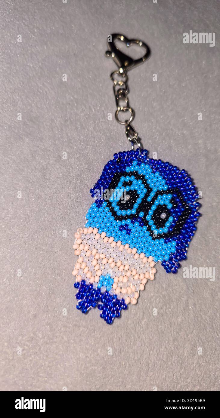 Ein Schlüsselanhänger in Form eines Zeichentrickfiguren, handgefertigt aus mehrfarbigen Perlen und Glasperlen auf grauem Hintergrund. Produktvorführung. Stockfoto