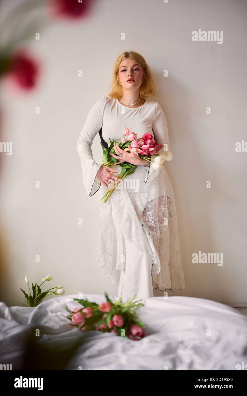 Frau in weißem Kleid, die Blumen in einer ruhigen Innenumgebung hält Stockfoto