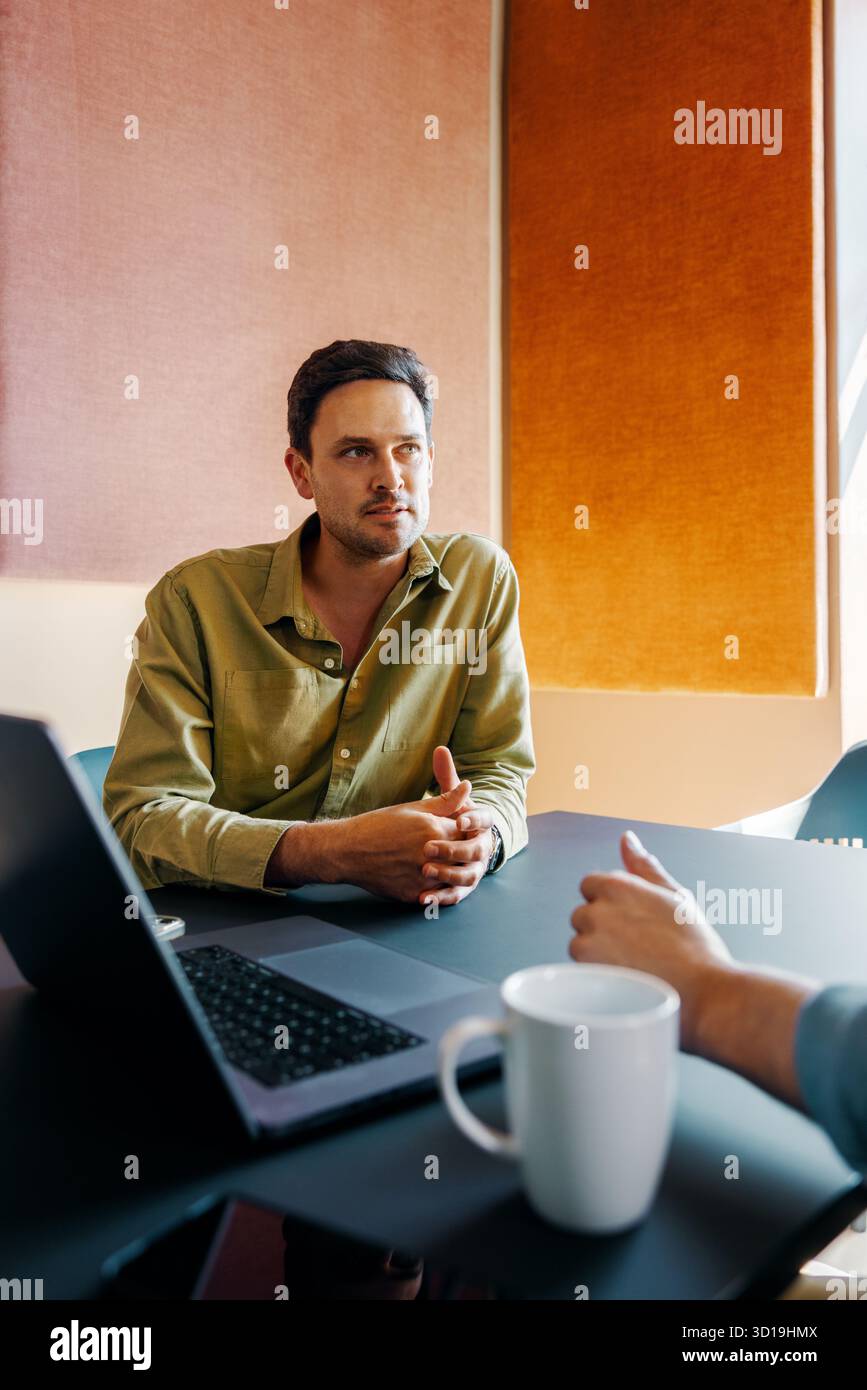 Junge Erwachsene diskutieren Ideen in einer gemeinsamen Büroumgebung mit lässiger Sitzanordnung und prominentem Laptop. Stockfoto