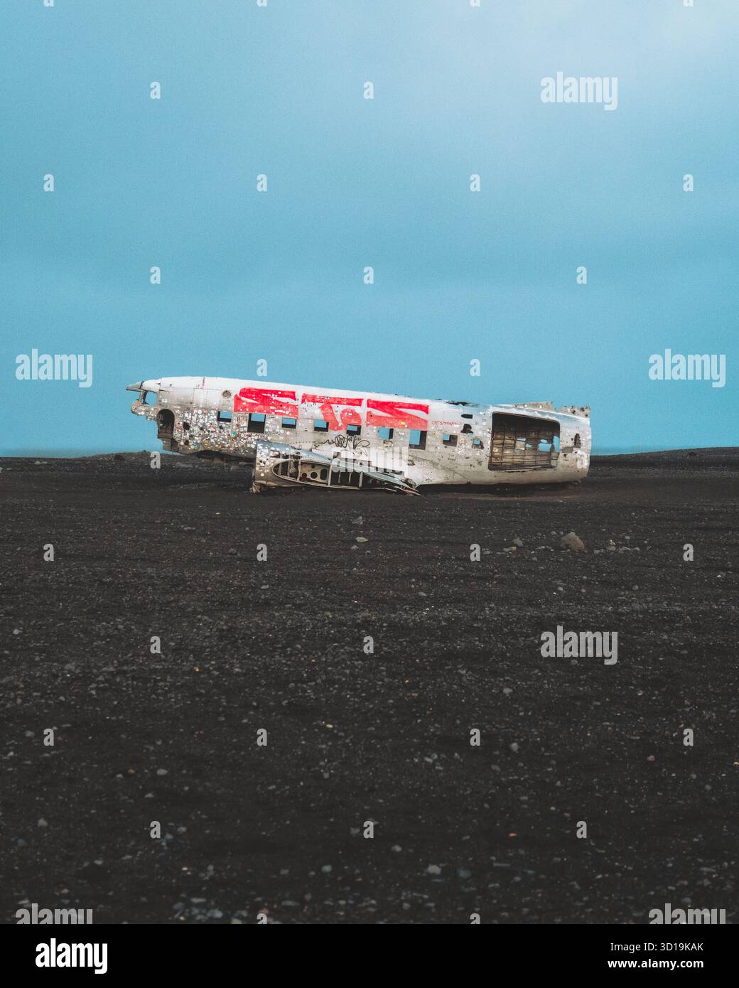 Blick auf ein verwittertes DC-3-Flugzeugwrack mit roten Akzenten auf einem schroffen schwarzen Sandstrand unter einem blassblauen Himmel, Solheimasandur Plane Wrack, Mýrdals Stockfoto