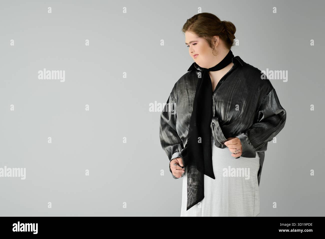 Eine junge Frau mit Down-Syndrom zeigt ihren Charme, während sie lächelt und ein schickes Outfit trägt. Stockfoto