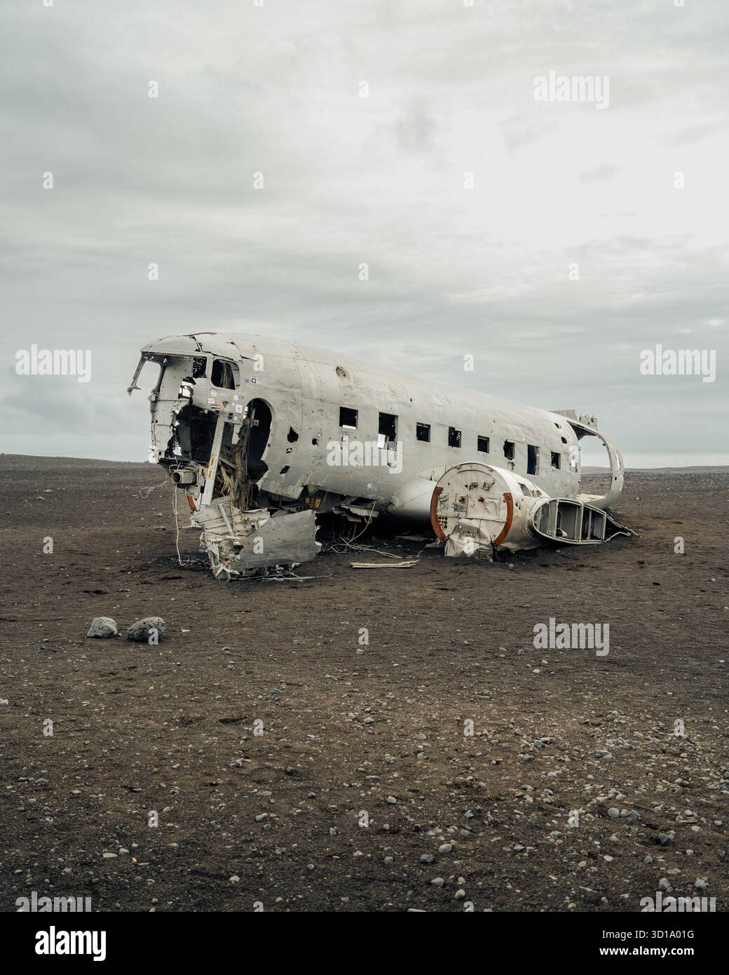Blick auf die Skelettreste eines DC-3-Flugzeugs, gebleicht durch die Zeit, ruhen auf dem krassen schwarzen Sand unter einem brütenden Himmel, eine eindringliche Szene, Sólheimasandur, Stockfoto