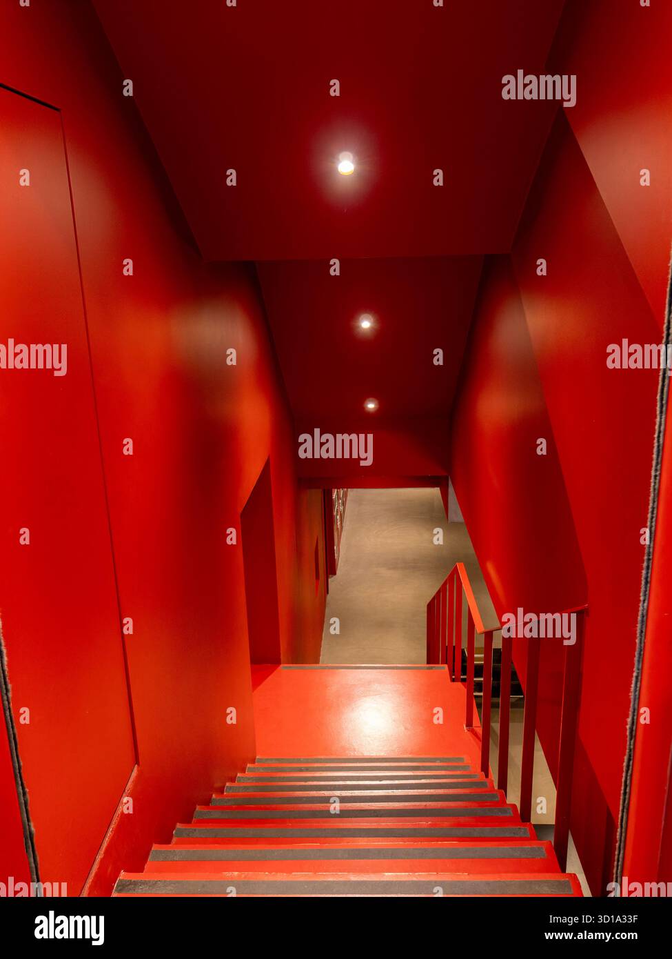 Rote Treppen und rote Wände, die gerade unter den Lichtern hinunterragen. Horror-Konzept mit roten Treppen. Stockfoto